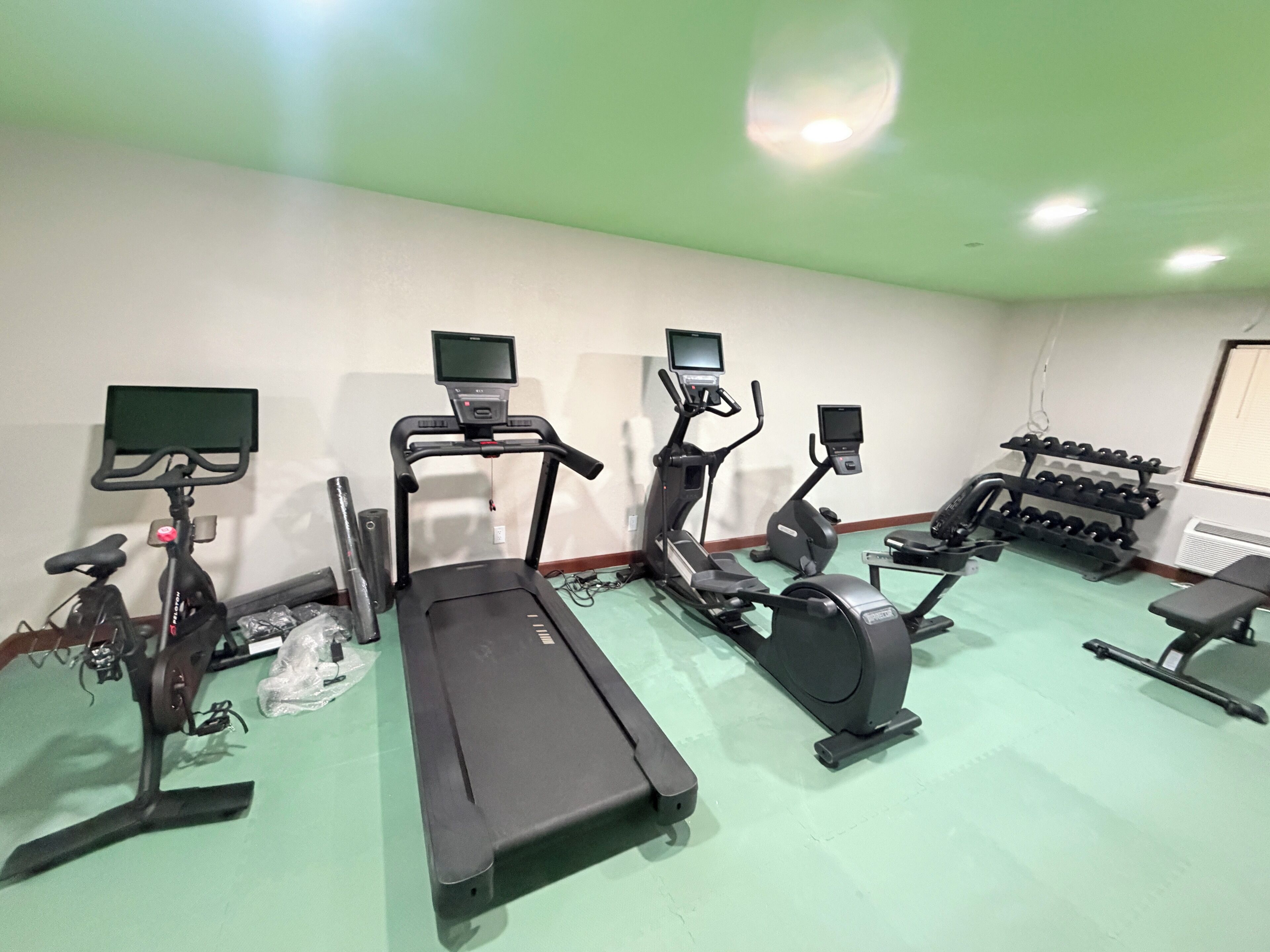 Un gimnasio con cintas de correr, elípticas y una banca.