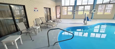 Una piscina interior con sillones de descanso, un letrero de salvavidas y grandes ventanales.
