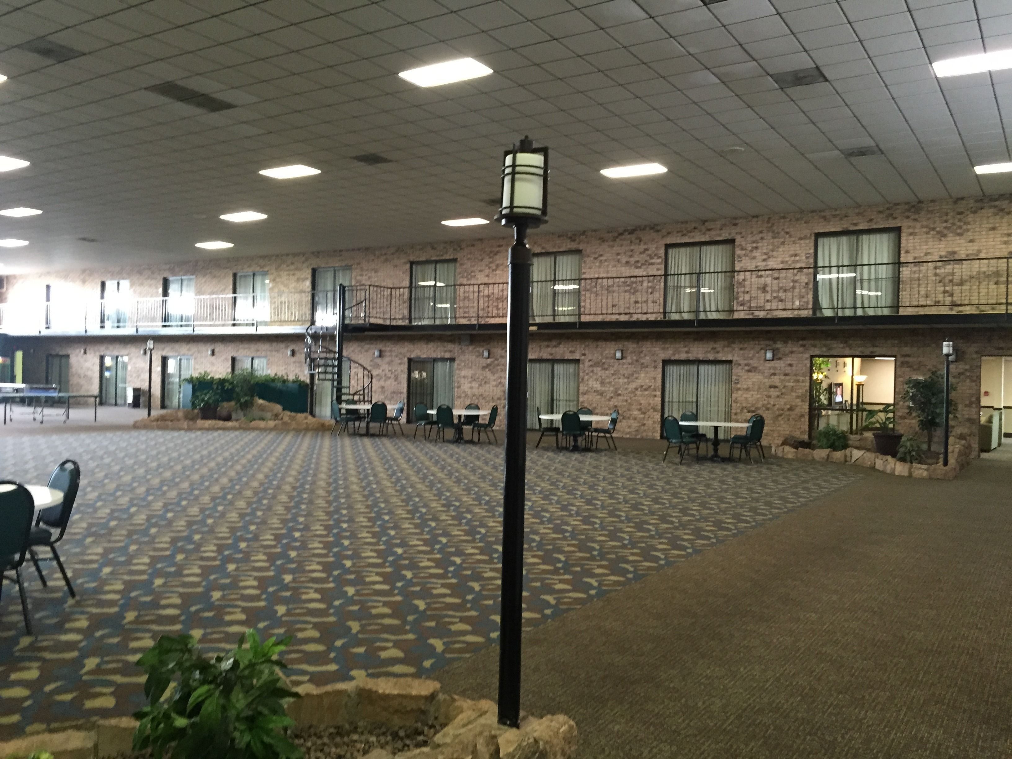 A spacious indoor area with a patterned floor, multiple tables and chairs, and a brick building with balconies.