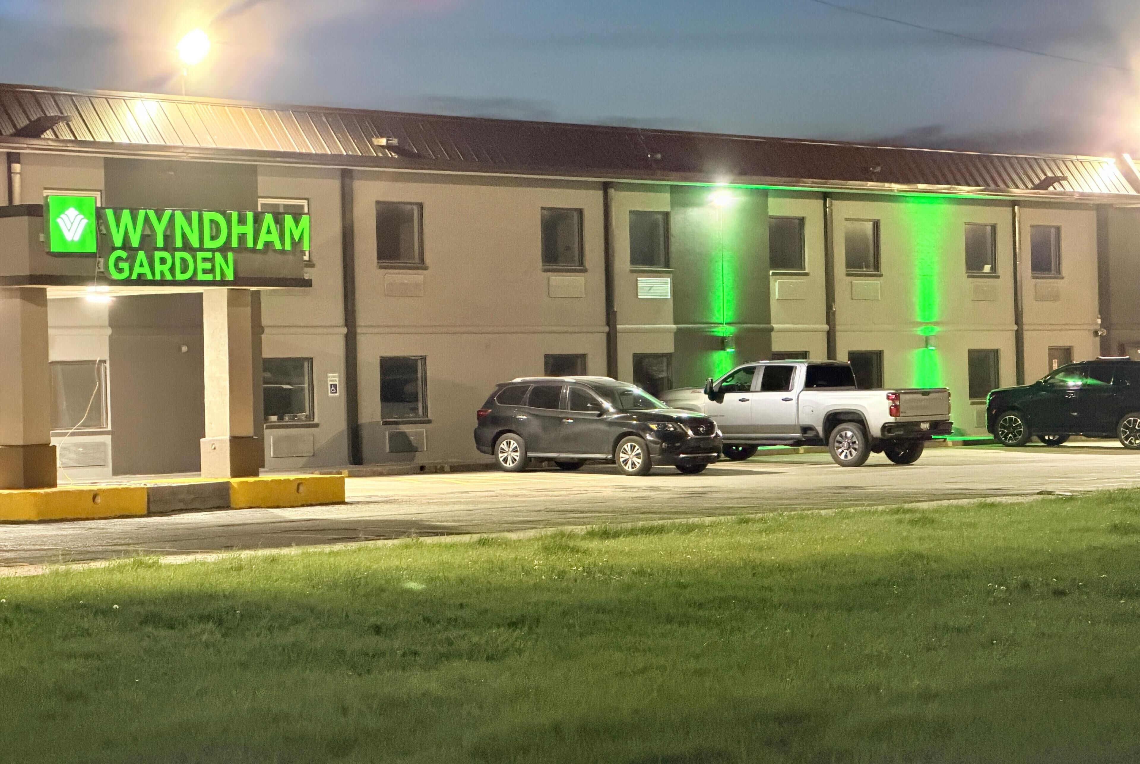 A building with a sign reading 'WYNDHAM GARDEN' and a parking lot with several vehicles.