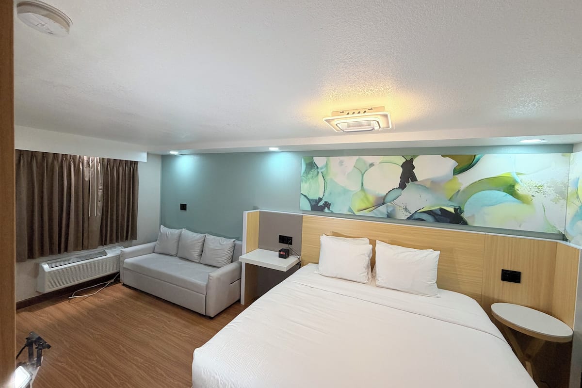 Habitació d'hotel amb un llit gran, un sofà, una taula petita, un radiador i una paret amb art abstracte.