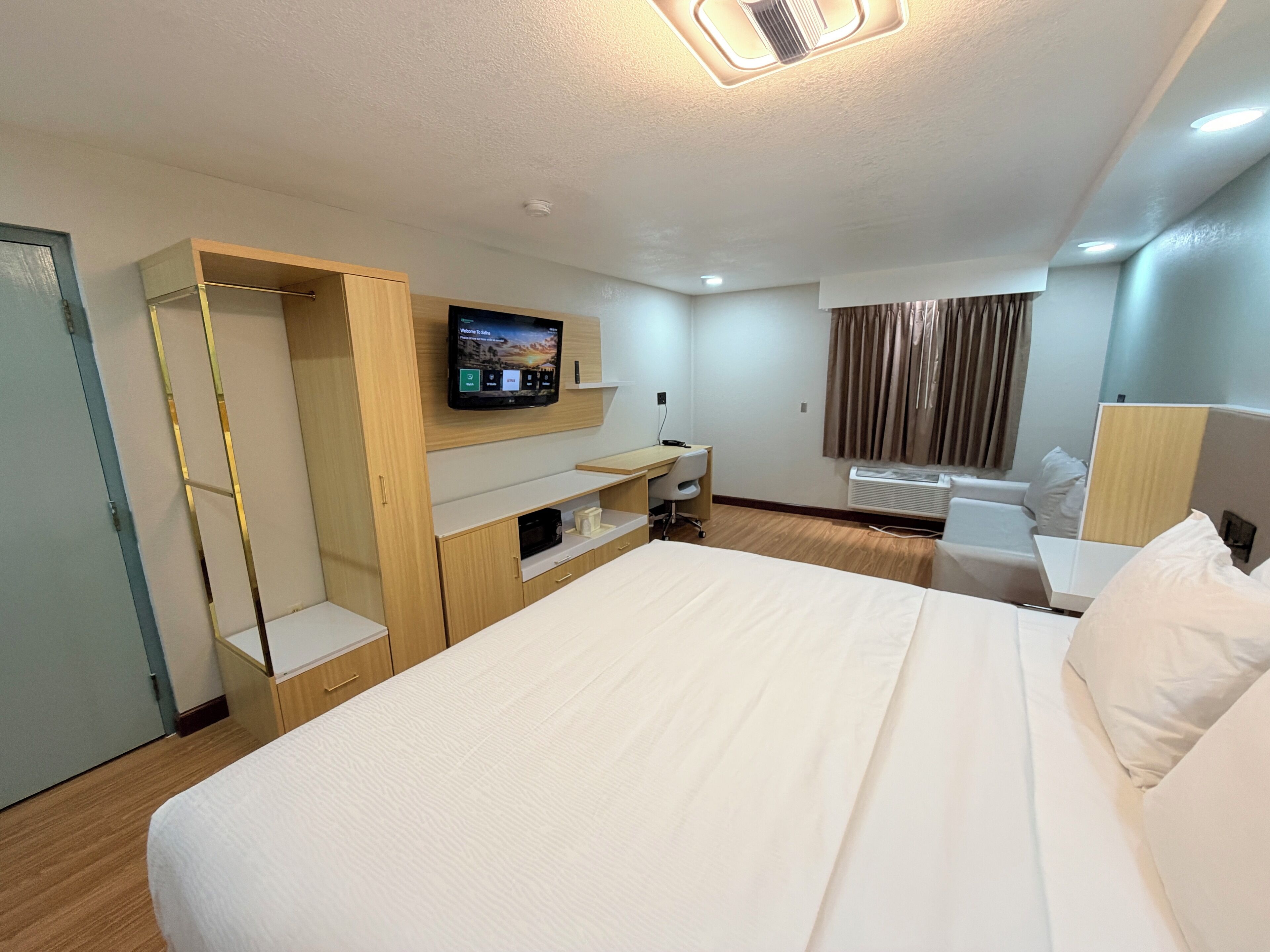 Habitación de hotel con cama, escritorio, televisión montada en la pared y ventana con cortinas.