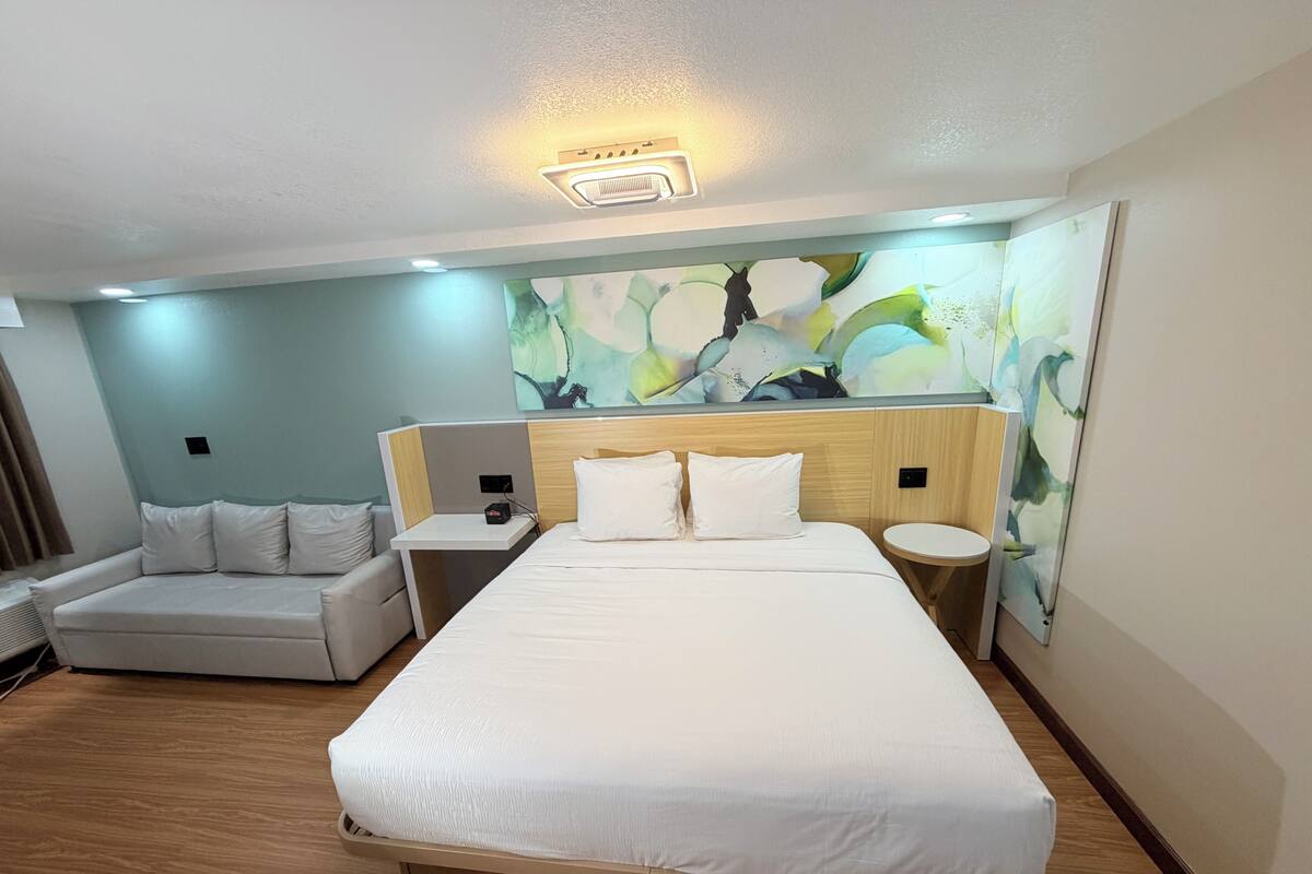 Habitació d'hotel amb un llit, una taula de nit, una cadira i una paret amb un mural floral.