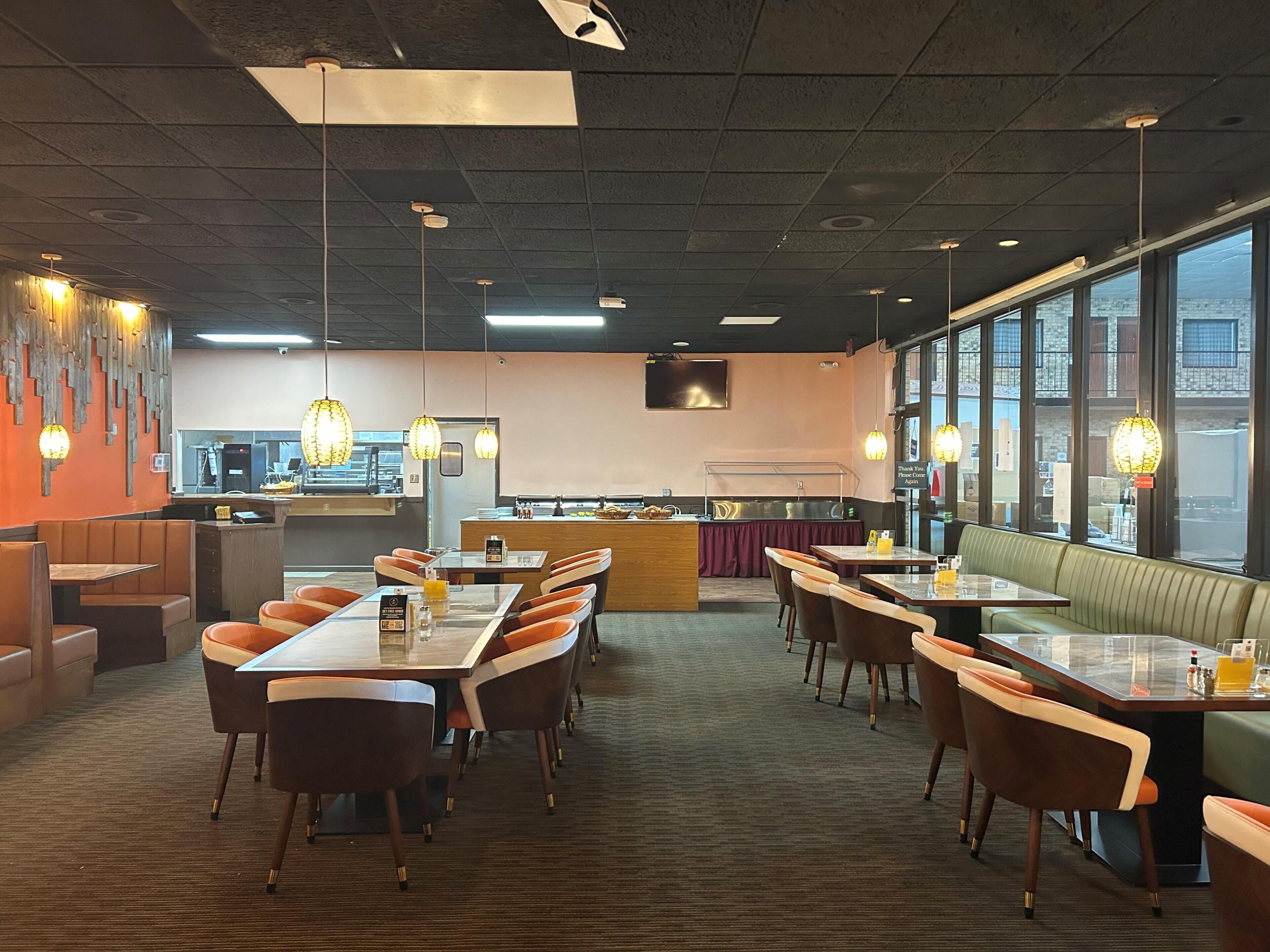 A restaurant with booths and tables, a kitchen in the background, and large windows.