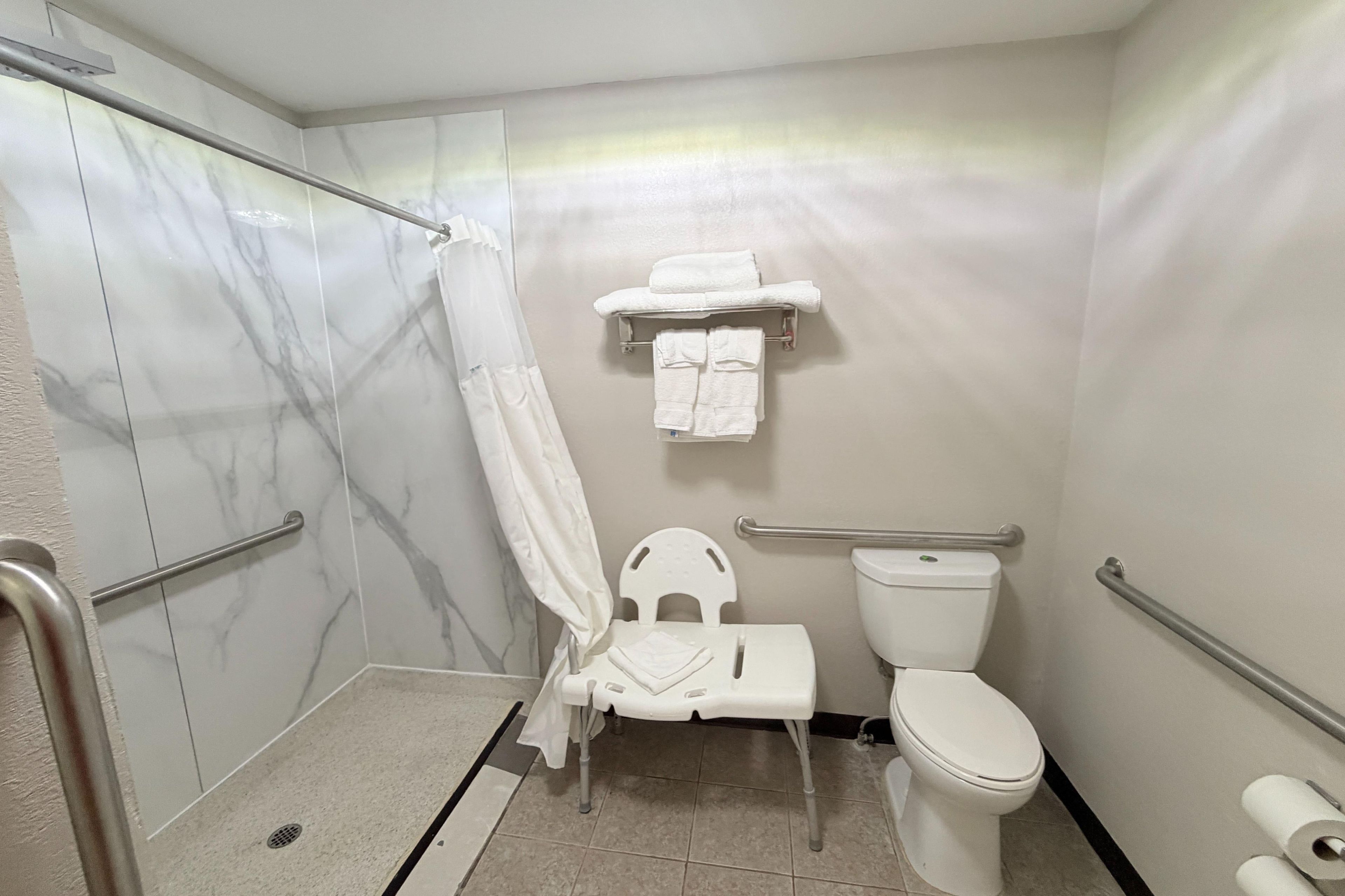 Un baño con ducha, inodoro y barras de apoyo.