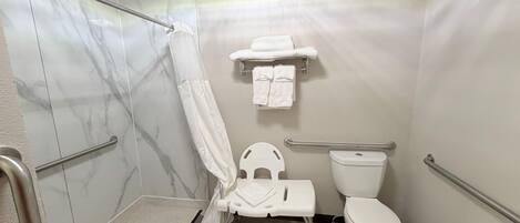 Un baño con ducha, inodoro y barras de apoyo.