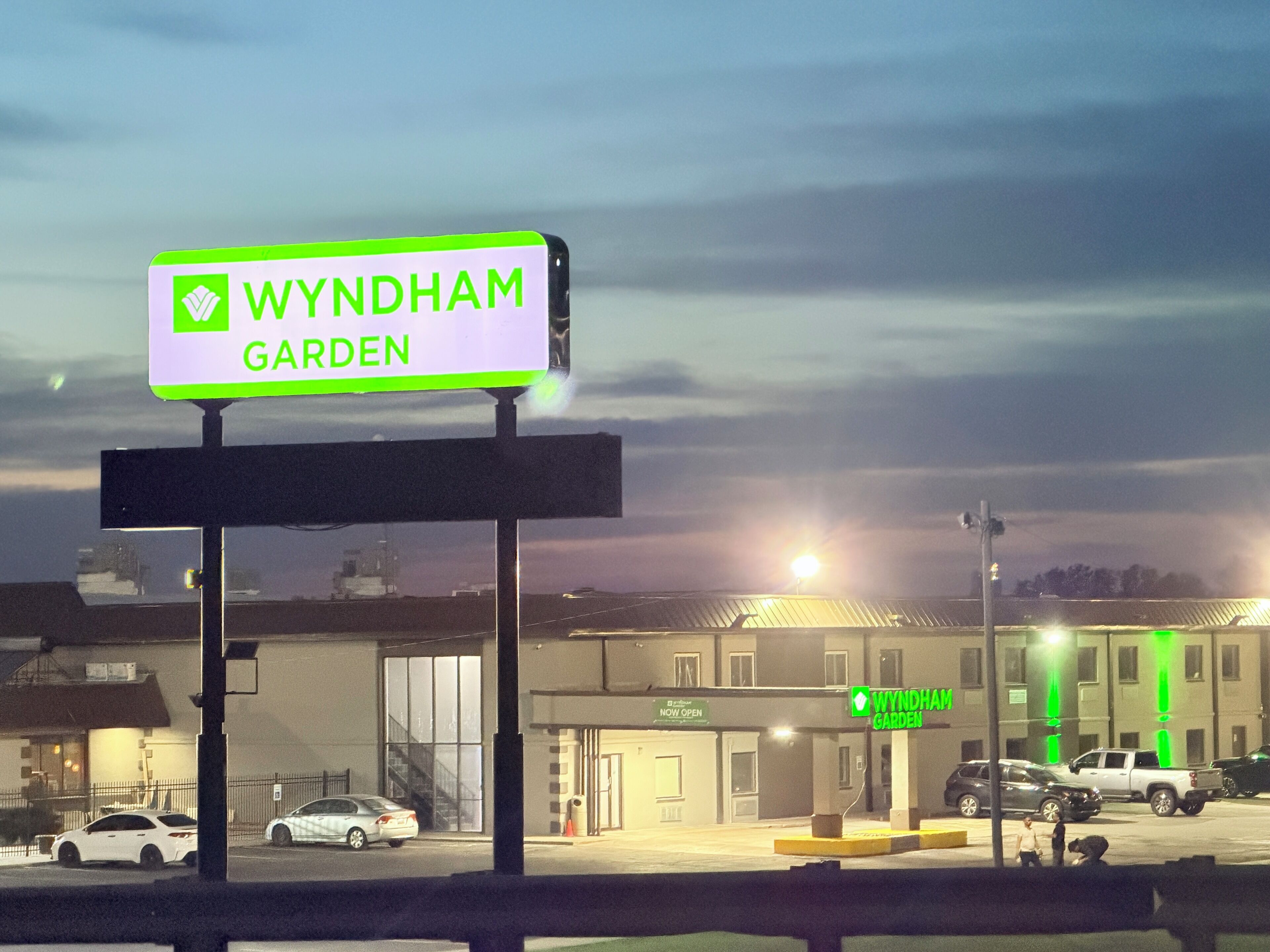 A sign for Wyndham Garden hotel, a parking lot, and a building with a 'NOW OPEN' sign.