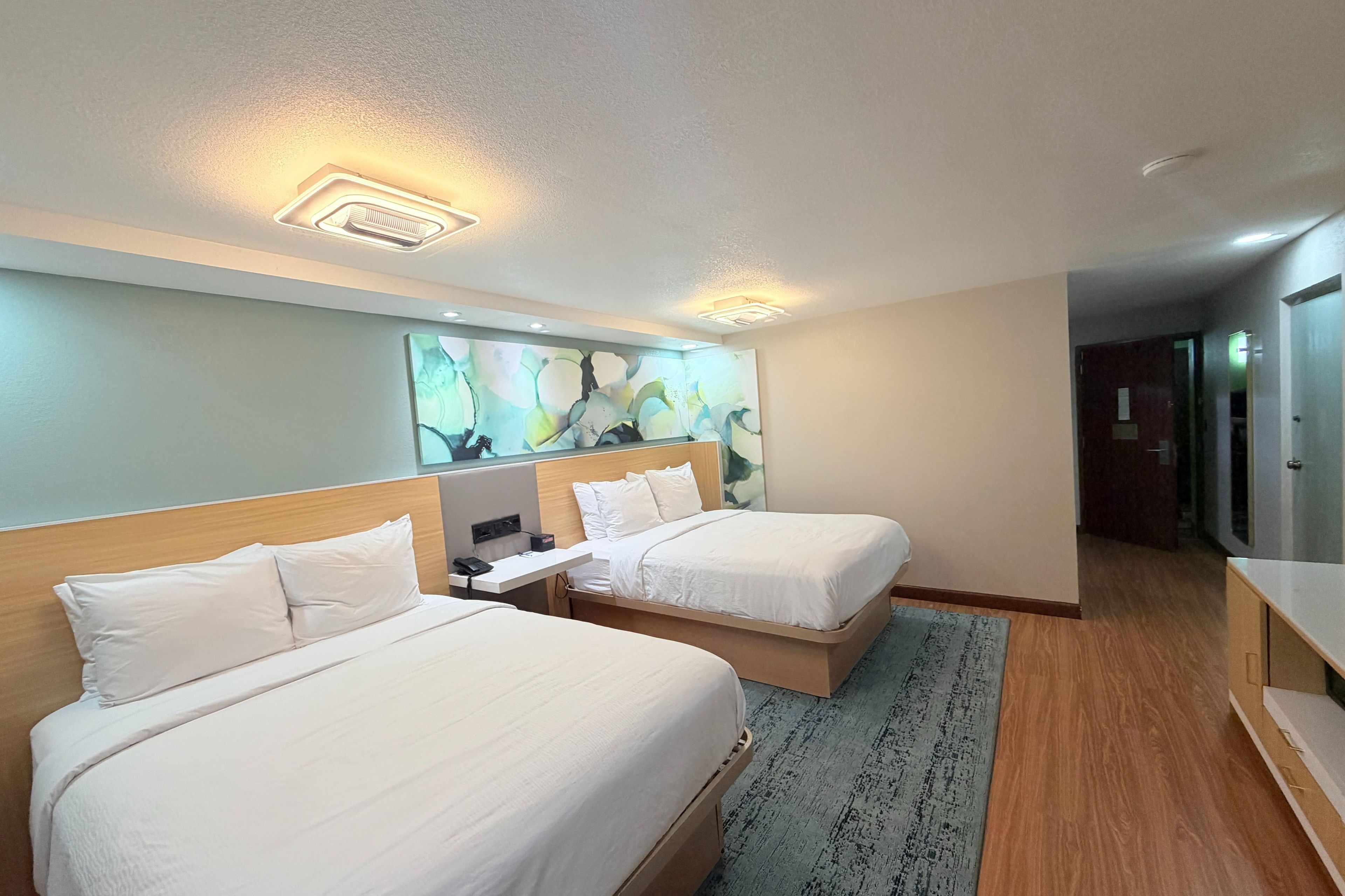 Habitación de hotel con dos camas, un escritorio, un televisor de pantalla plana y una lámpara de techo moderna.
