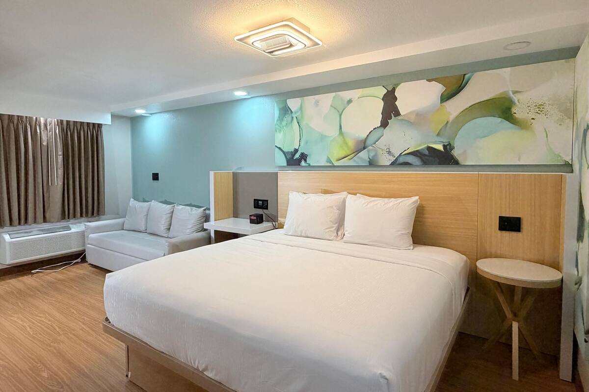 Habitació d'hotel amb un llit gran, un sofà, una taula petita i una obra d'art penjada a la paret.