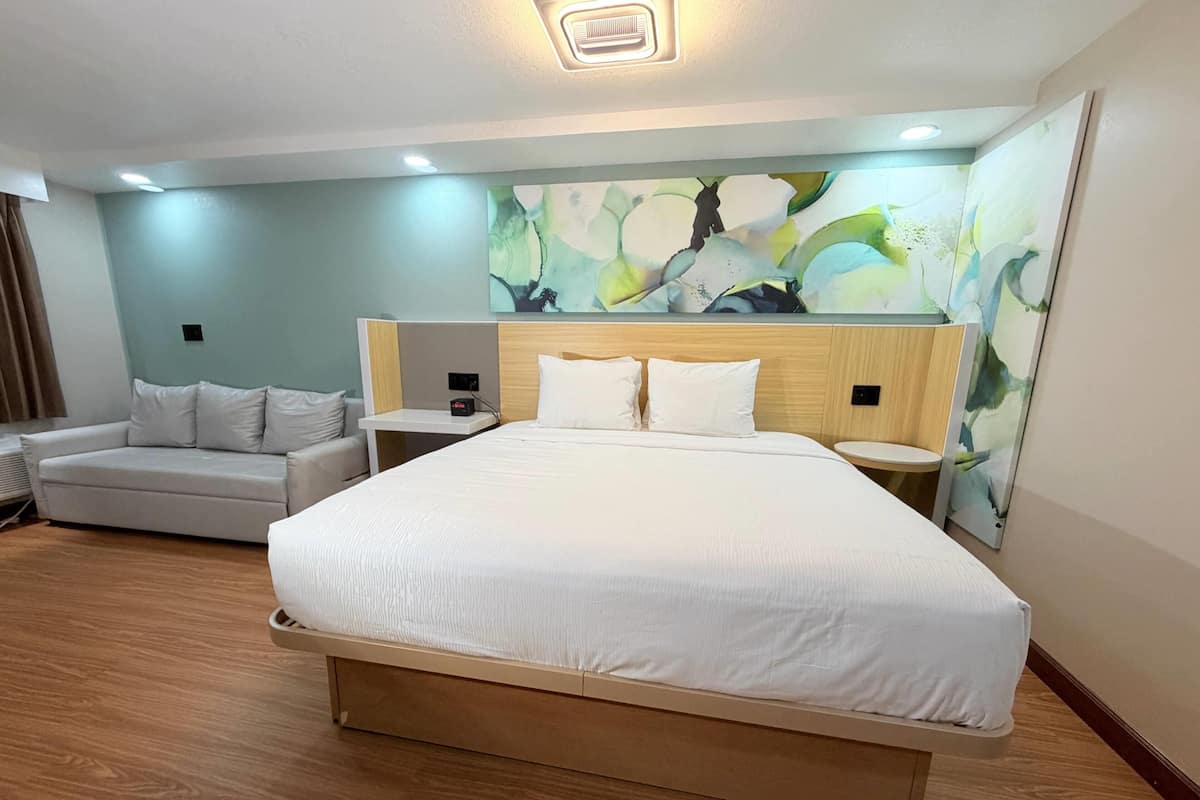 Una habitació d'hotel amb un llit gran, un sofà, una tauleta de nit i una obra d'art penjada a la paret.