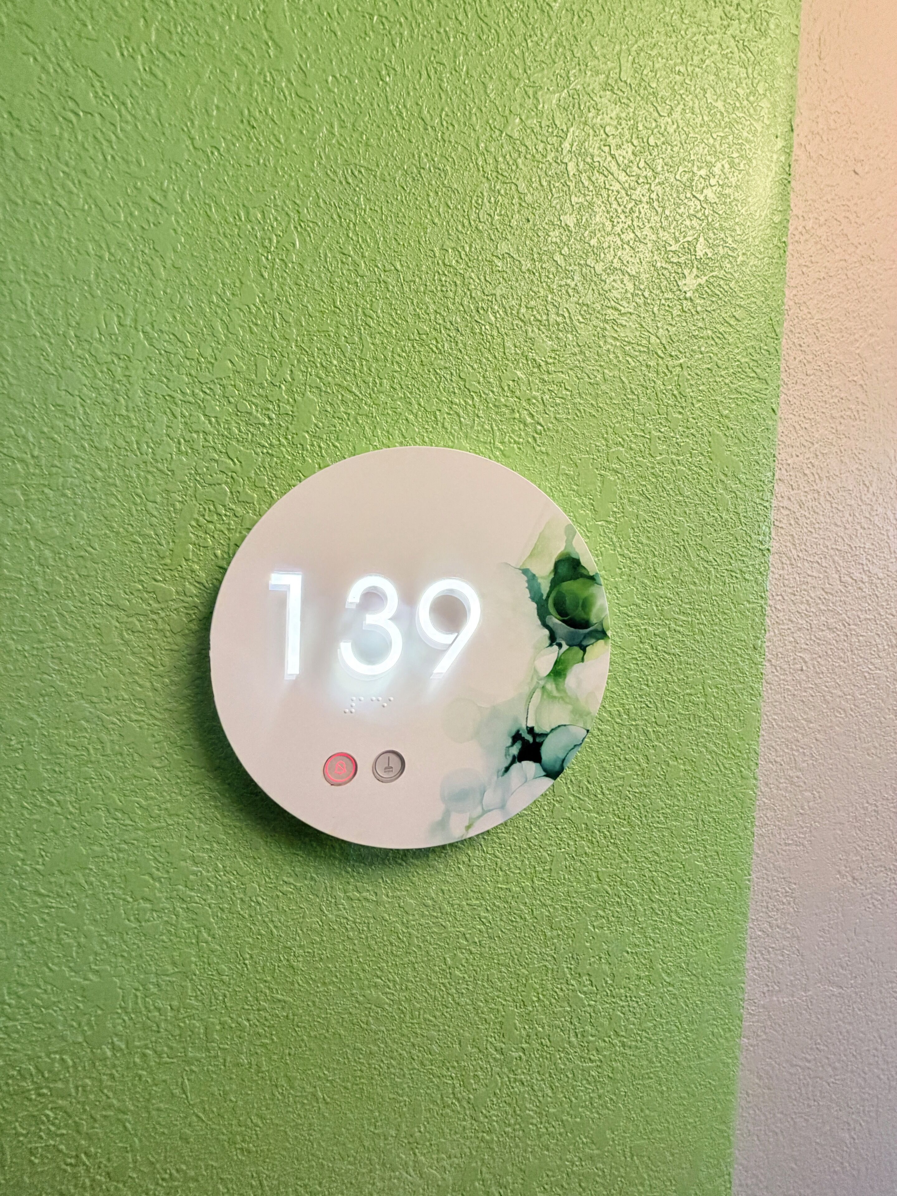 A round, white sign with the number 139 on a textured green wall.