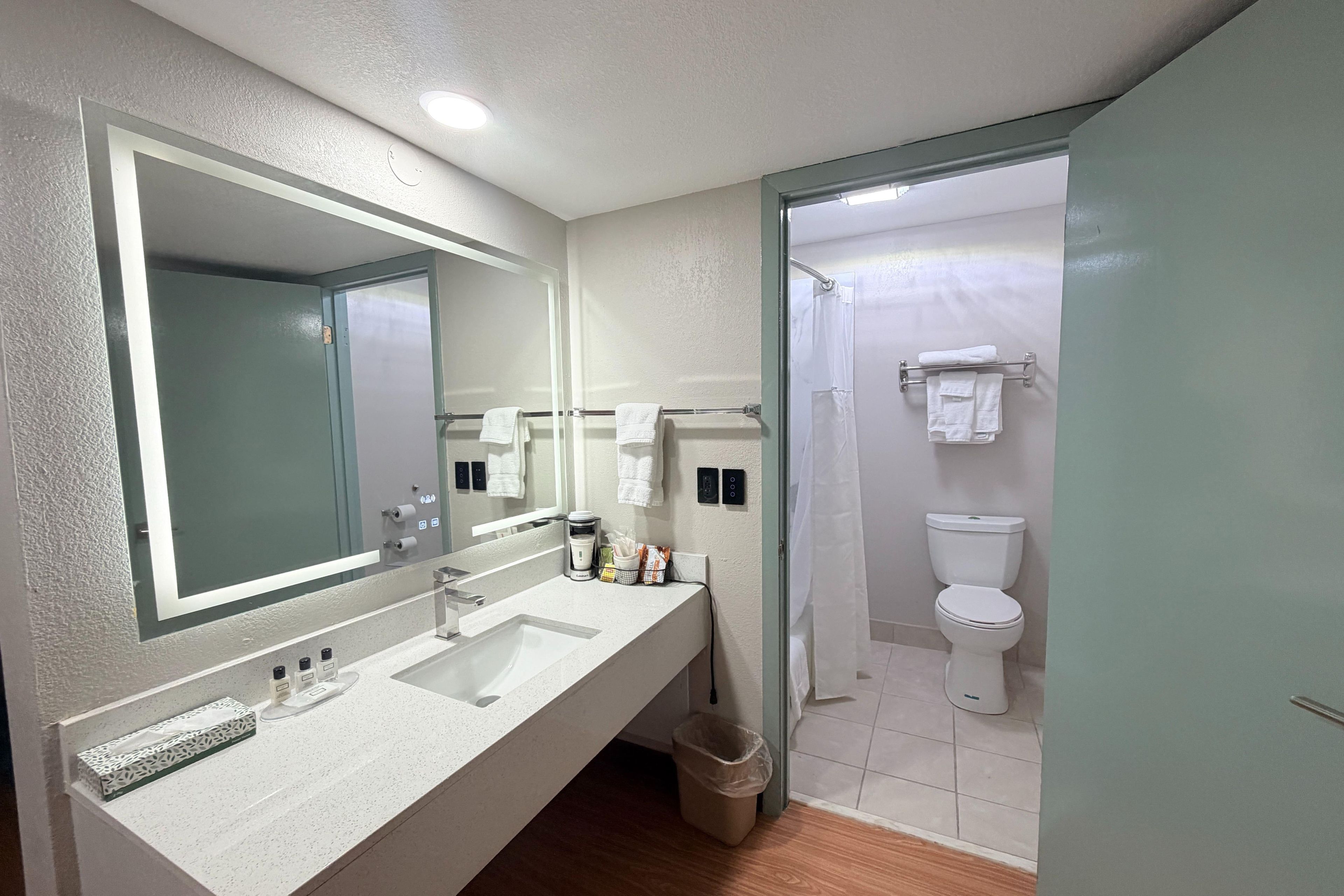 A modern bathroom with a large mirror, a sink, a toilet, and a shower area.