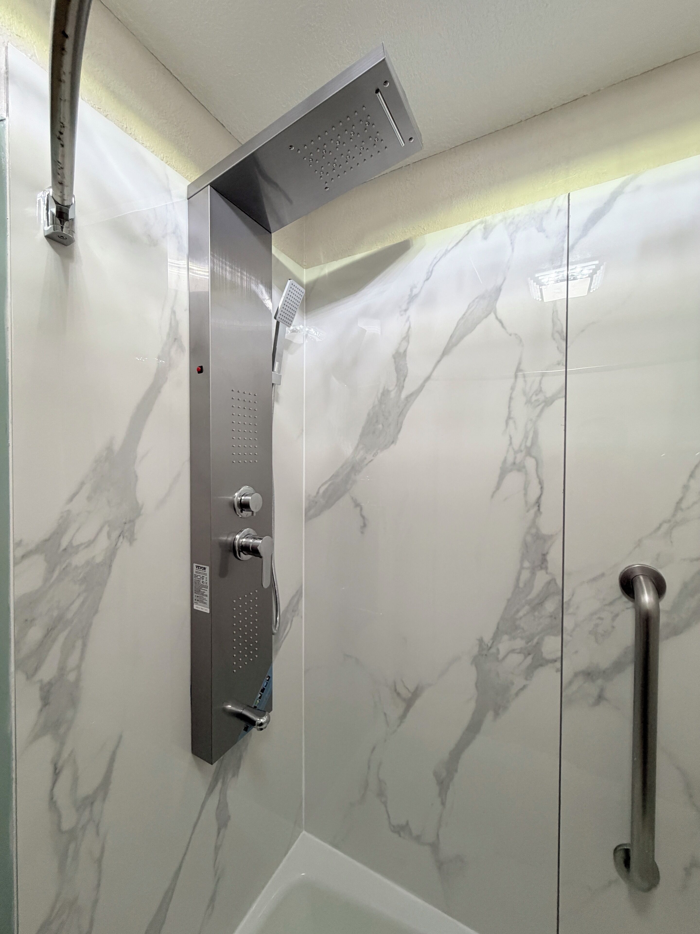 Een douche met een handdouche, bedieningspaneel aan de muur en een handgreep.