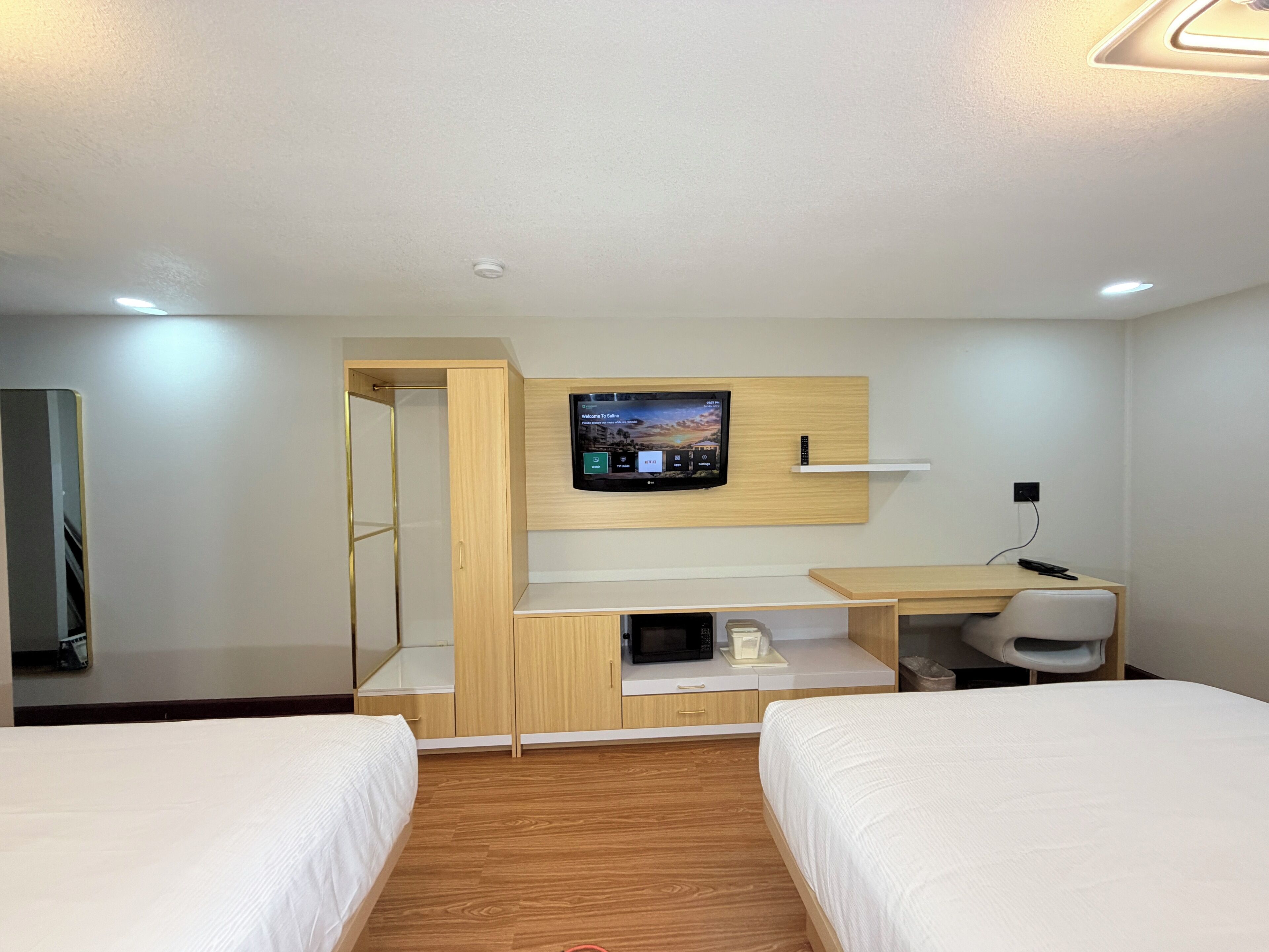 A hotel room with two beds, a TV mounted on the wall, a desk with a chair, and a microwave.