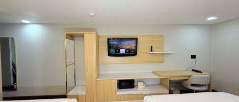 A hotel room with two beds, a TV mounted on the wall, a desk with a chair, and a microwave.