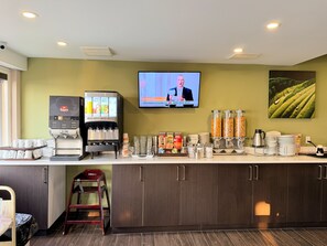 A coffee station with a coffee machine, condiment dispensers, and a television displaying a news program. - Sleep Inn & Suites Quebec City East (Boischatel)