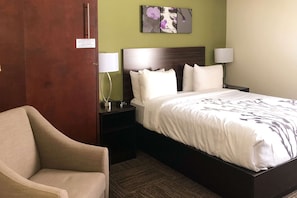 A hotel room with a bed, two bedside tables, a chair, and a wall with a floral painting.