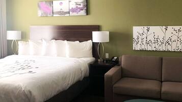 Una habitación de hotel con una cama grande, dos lámparas de noche, un sofá marrón y una pequeña mesa redonda.
