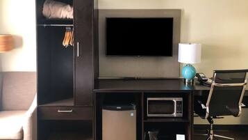 Quarto de hotel com guarda-roupa, televisão de tela plana, escrivaninha com luminária, micro-ondas e uma cadeira.