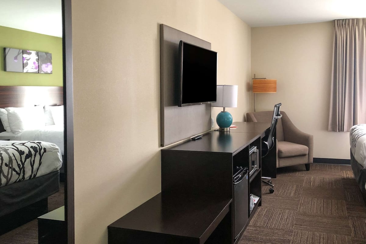 A hotel room with a bed, a desk, a chair, a television, and a lamp.