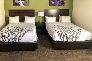 A hotel room with two beds, each with a dark headboard and white bedding with a floral pattern. There is a nightstand with a lamp between the beds, and the walls are painted green. - Sleep Inn & Suites Quebec City East (Boischatel)
