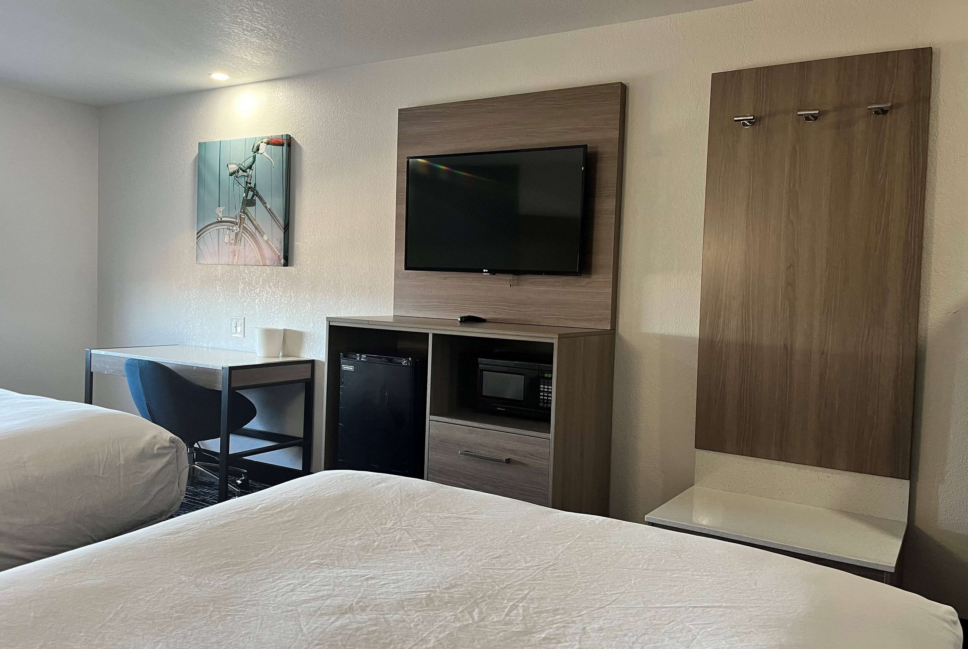 A hotel room with two beds, a desk with a chair, a television, a microwave, and a wardrobe.