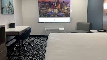 Habitación de hotel con cama, escritorio, silla, ventana con vista panorámica de la ciudad y unidad de aire acondicionado.