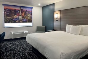 Una habitación de hotel con una cama grande, una silla, un escritorio, una lámpara y un cuadro de un paisaje urbano.