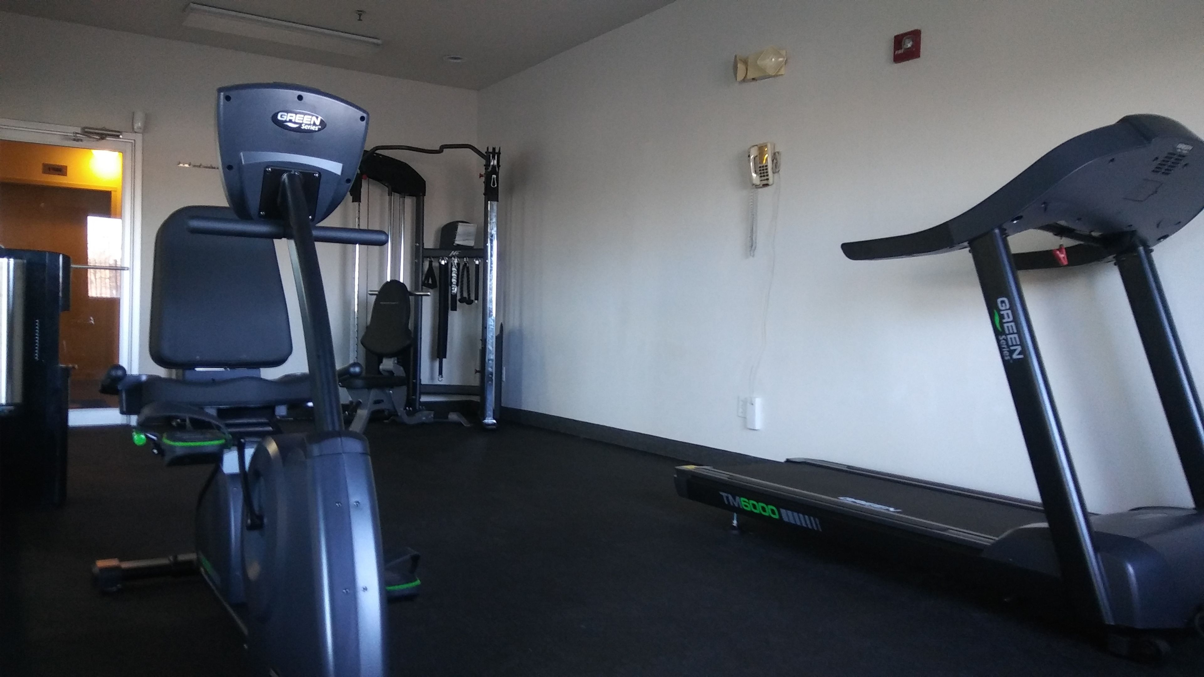 Un gimnasio con equipo de cardio, una banca para pesas y una máquina de ejercicio de pared.