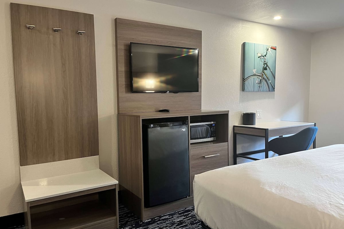 Habitación de hotel con una cama, un escritorio con silla, un televisor montado en la pared, un refrigerador y un microondas.