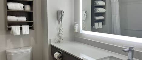 Un baño con inodoro, un estante con toallas, un secador de pelo y un lavamanos con espejo.