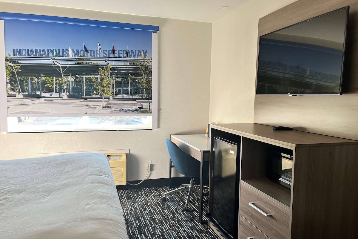 Habitación de hotel con cama, escritorio, televisión y un cartel del Indianapolis Motor Speedway.