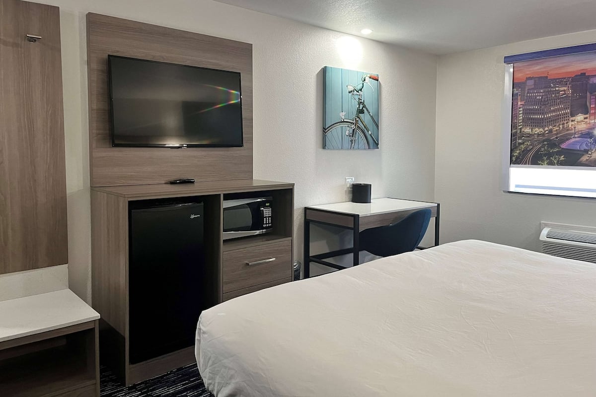 Una habitación de hotel con cama, escritorio, televisor, microondas y refrigerador pequeño.