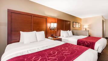 Habitación de hotel con dos camas, cabecero de madera, mesita de noche con lámpara y una manta roja.