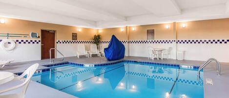 Una piscina interior con carriles delimitados, una silla de socorrista y una zona de estar cubierta.