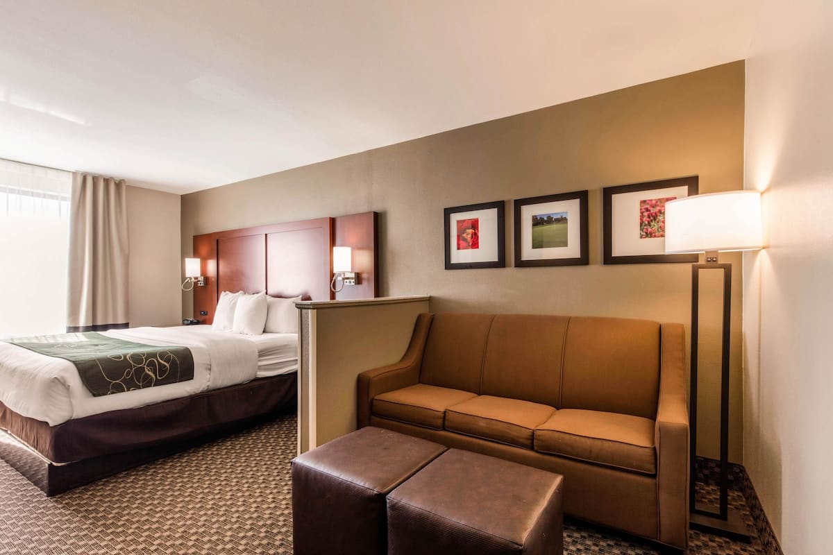 A hotel room with a bed, a sofa, a coffee table, and framed pictures on the wall.