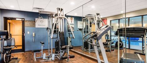 Une salle de sport équipée de machines de cardio, de postes d’entraînement avec poids et d’un mur recouvert de miroirs.