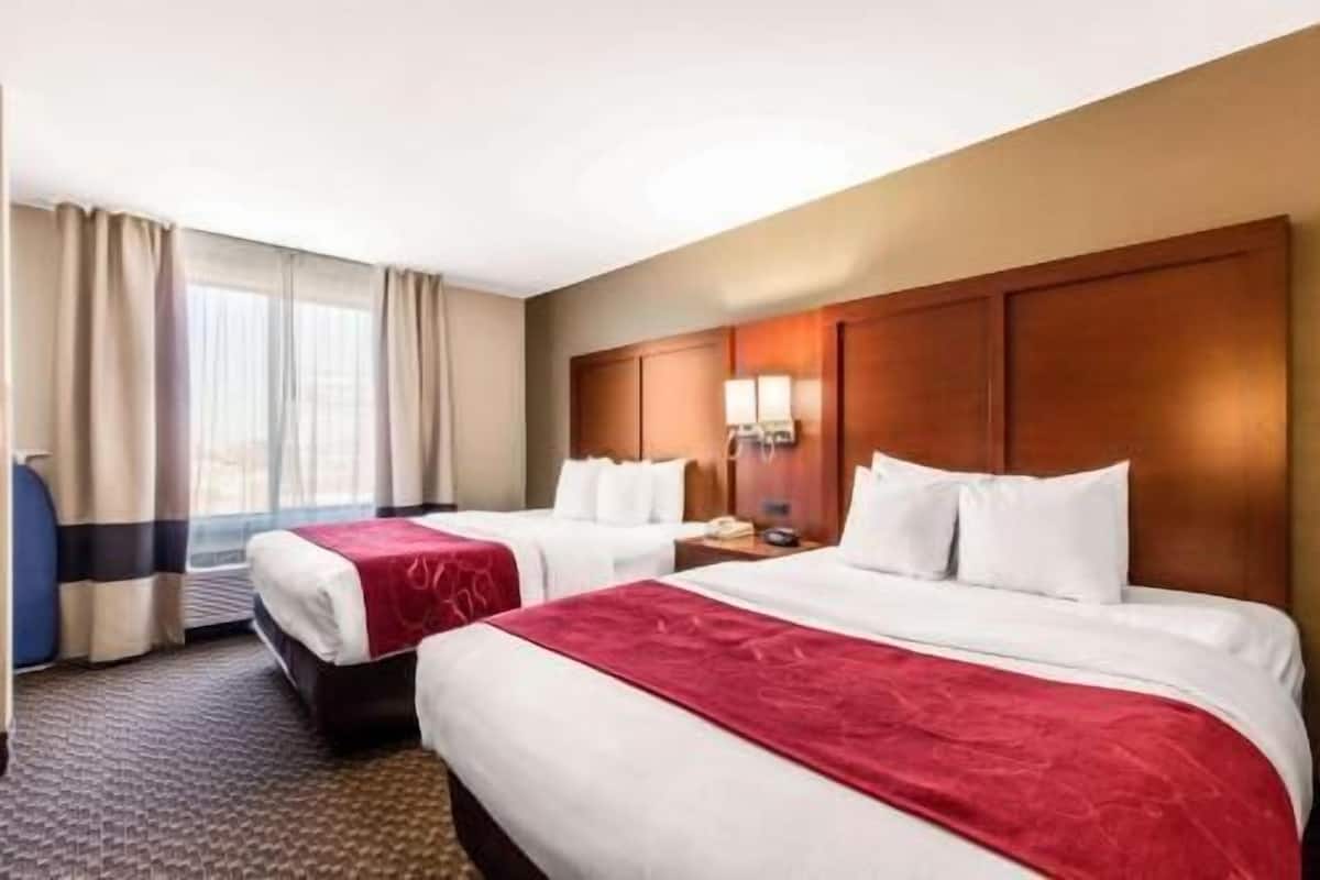 A hotel room with two beds, a wooden headboard, a nightstand, and a window with curtains.