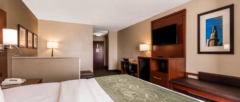 A hotel room with a bed, a desk, a chair, a TV, and a sofa.