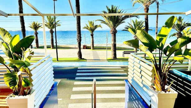 A view from a balcony overlooking a beach with palm trees and a clear sky. - Hotel Neptuno (San Pedro del Pinatar)