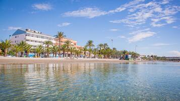 A beachfront hotel with a clear view of the sea, palm trees, and a sandy beach.