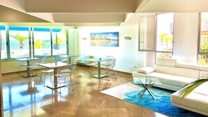 A modern living room with a large window, a white sofa, and a dining area with metal chairs and a glass table. - Hotel Neptuno (San Pedro del Pinatar)