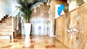 A marble-floored lobby with a large potted plant, a staircase, and a wall with a compass design. - Hotel Neptuno (San Pedro del Pinatar)