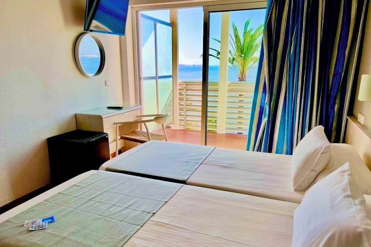 A hotel room with two beds, a desk, a chair, and a TV.