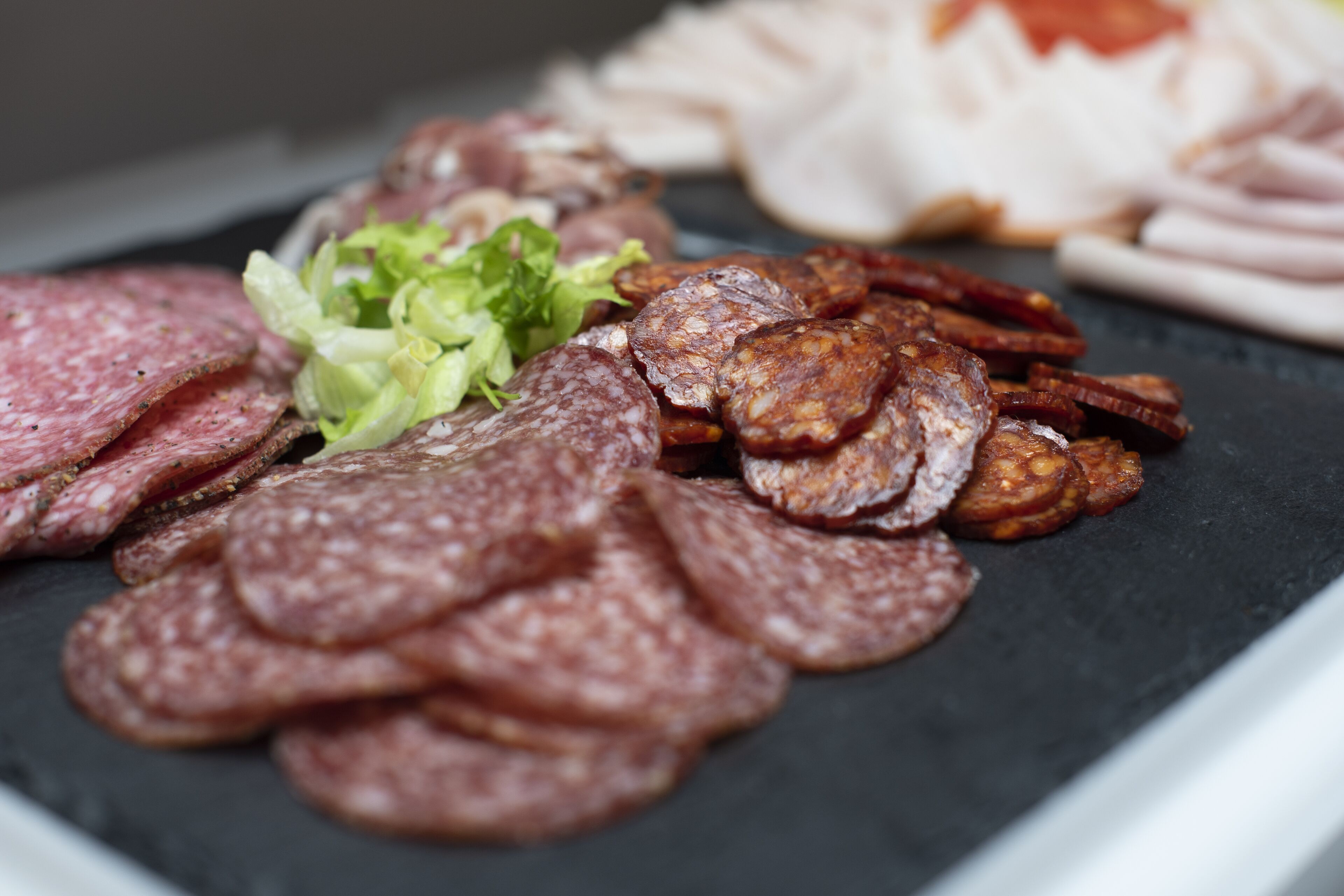 A variety of sliced meats on a black slate surface.