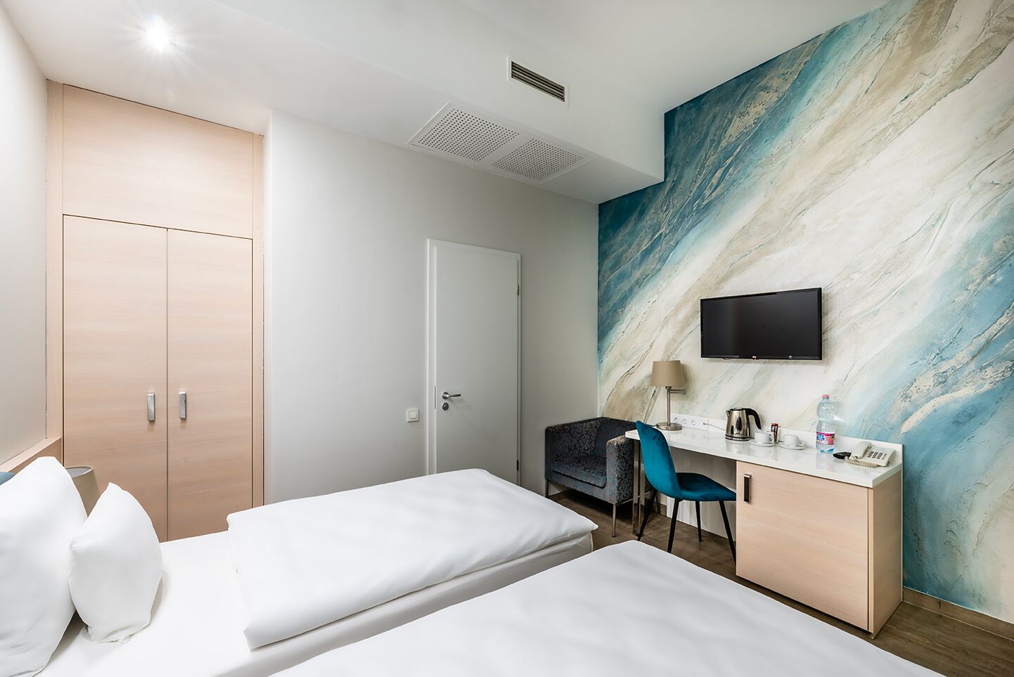 Ein Hotelzimmer mit zwei Betten, einem Schreibtisch mit Stuhl, einem Fernseher und einem großen abstrakten Gemälde an der Wand.
