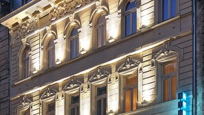 Een meerhoog gebouw met verfijnde architectonische details, waaronder gebogen ramen en decoratieve ornamenten. Een bord wijst ernaar dat het een hotel is, met een neonreclame aan de rechterkant.