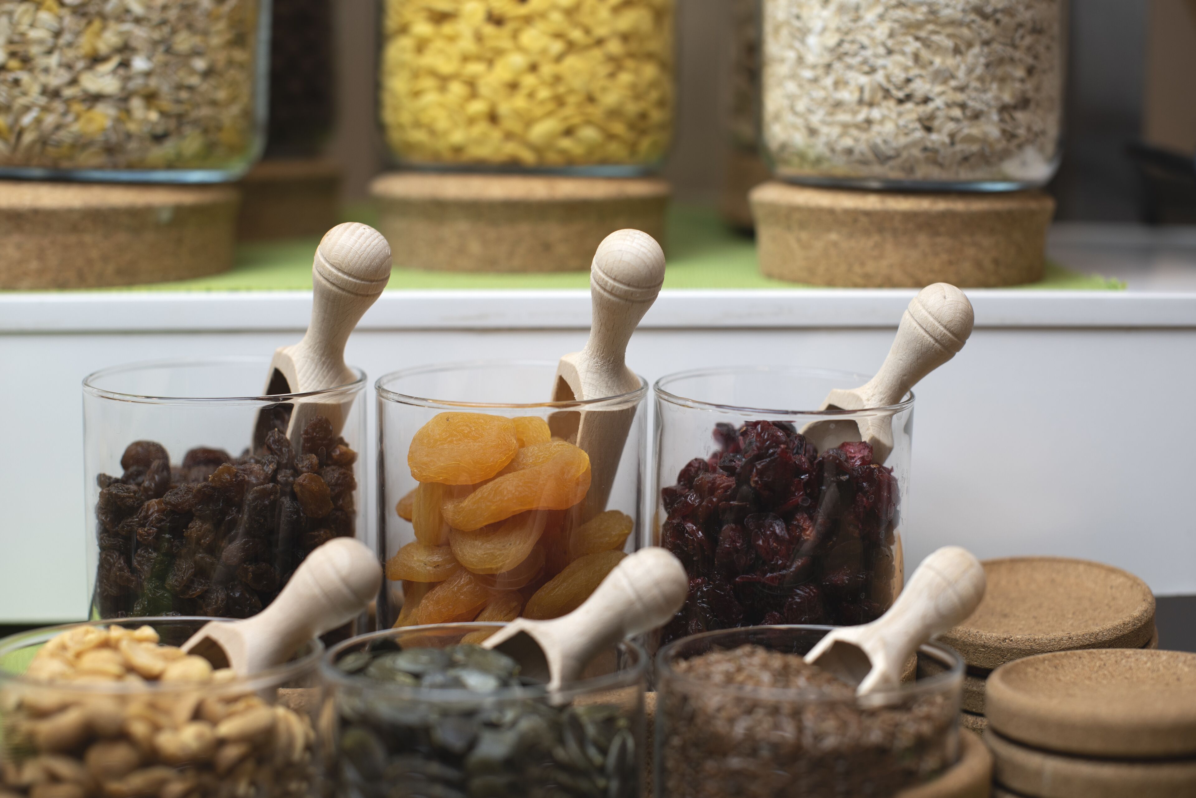 A display of various dried fruits and nuts in glass containers with wooden scoops.
