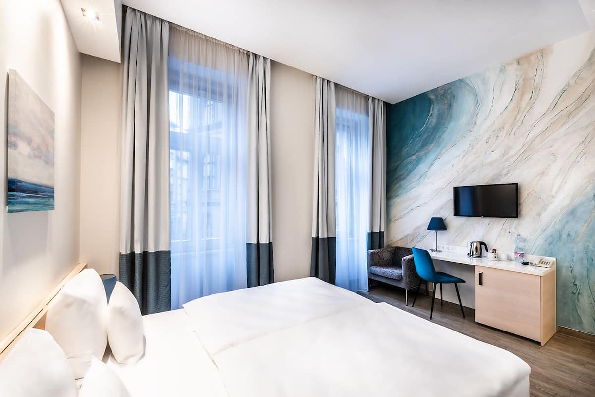 Hotellihuone, jossa on suuri sänky, työpöytä tuolilla, taulutelevisio ja marmoriseinä.