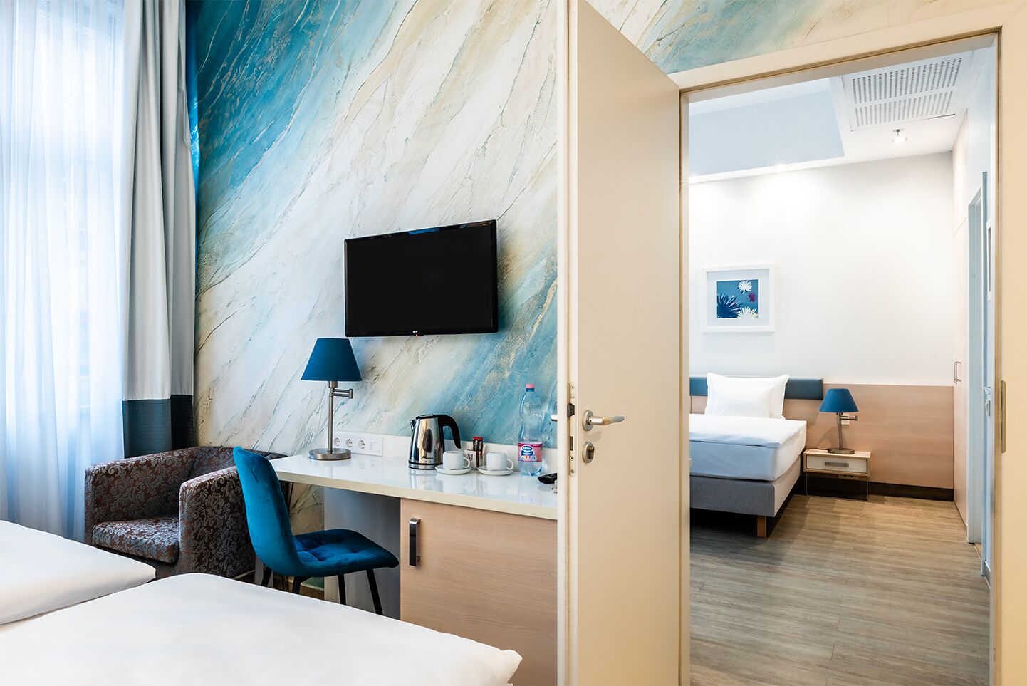 Habitación de hotel con pared de mármol, televisor de pantalla plana, escritorio con lámpara, una silla y cama con mesita de noche.